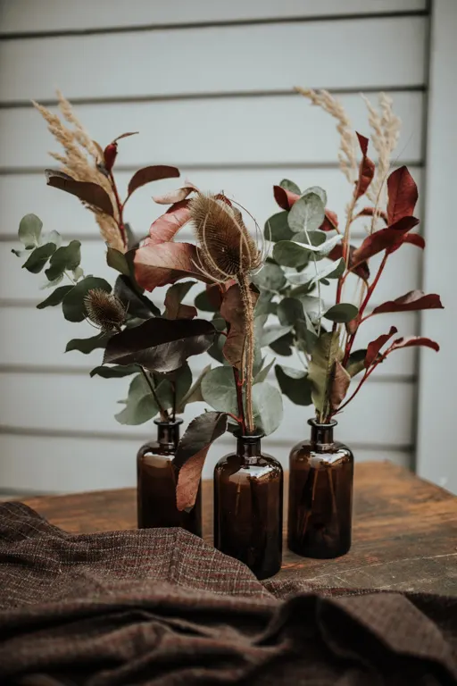 Glatte braune Apothekerflaschen mit Trockenblumen und Eukalyptus auf einem Holztisch