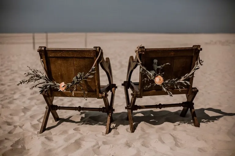 Brautpaarstühle mieten Zwei dunkle Brautpaarstühle mit Olivenzweigen im Sand am Strand