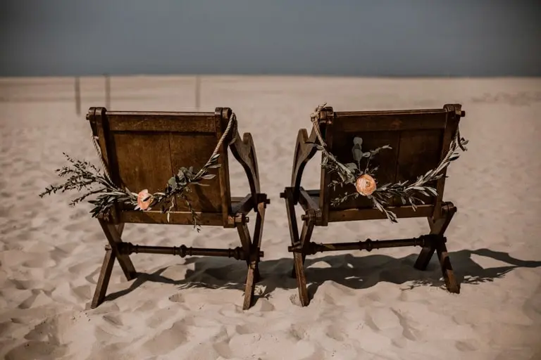 Zwei dunkle Brautpaarstühle mit Olivenzweigen im Sand am Strand