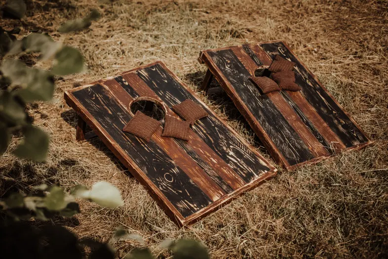Zwei Cornhole Bretter aus dunklem Holz mit Wurfsäckchen auf Stroh