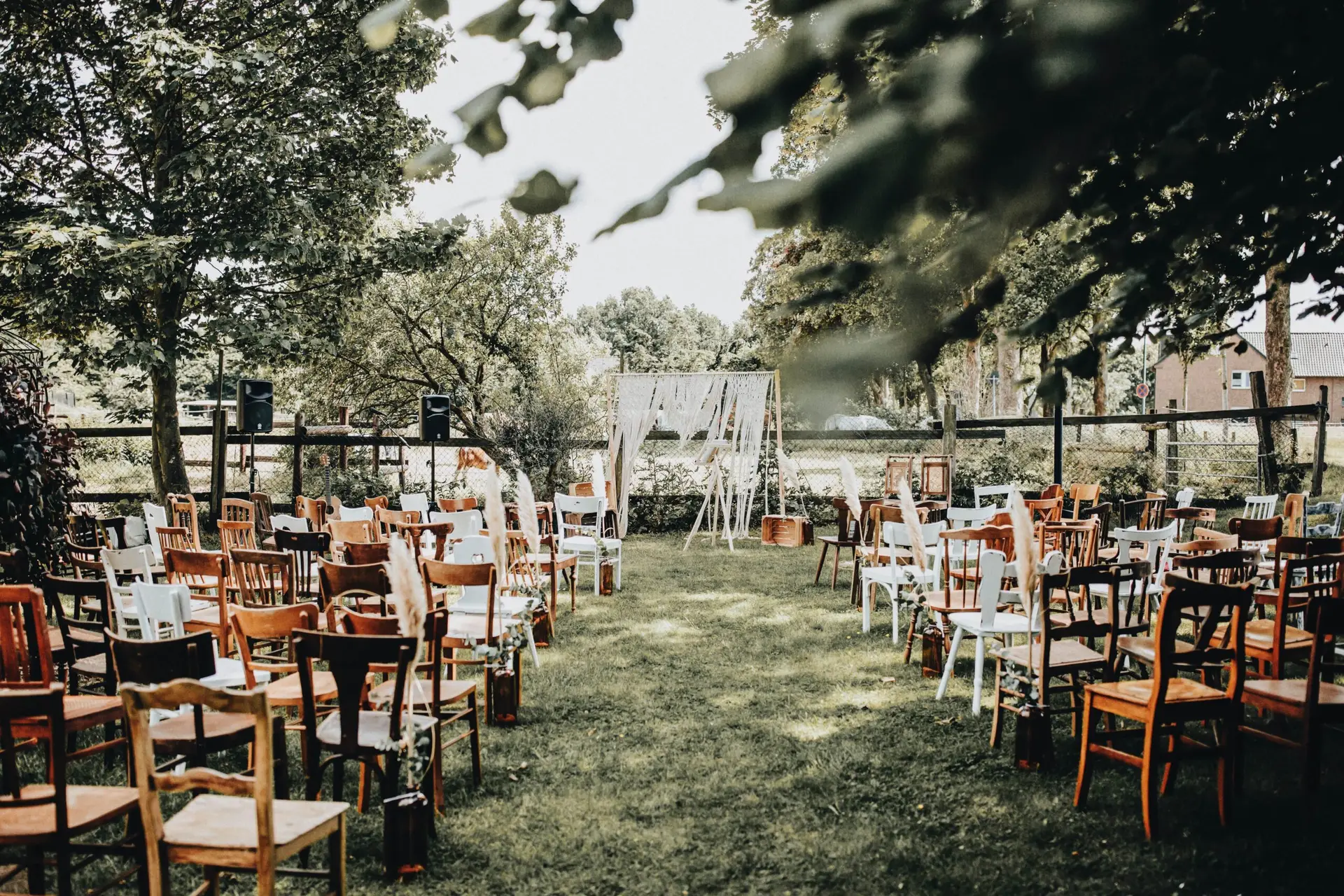 Lange Holztafeln mit Stühlen unter Bäumen bei einer Gartenhochzeit