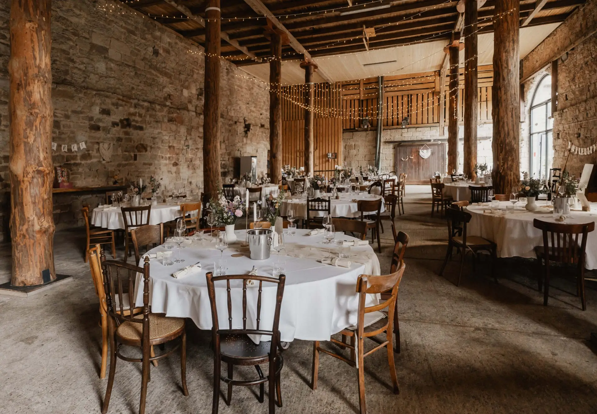 Rundtische mit weißen Decken und Holzstühlen in einer alten Halle