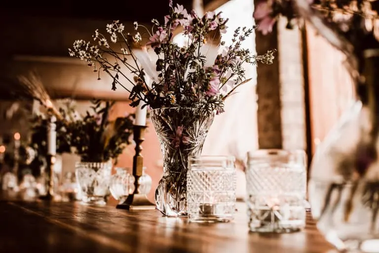 Glasset mit Wiesenblumen und Kerzen bei Abendlicht