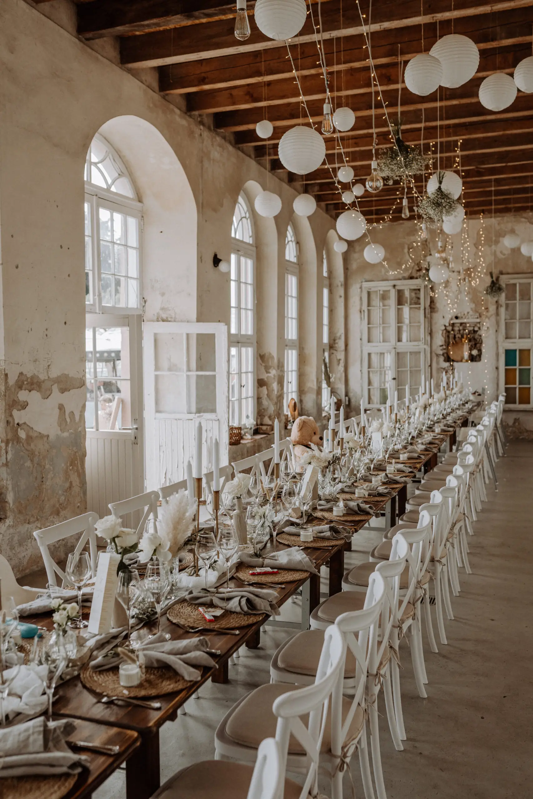 Lange Tafel mit weißen Stühlen in einer hellen Halle mit Rundbogenfenstern