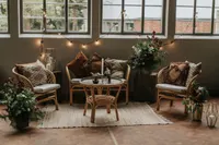 Lounge aus Rattansesseln, Sitzbank und rundem Tisch mit Kissen vor Sprossenfenstern