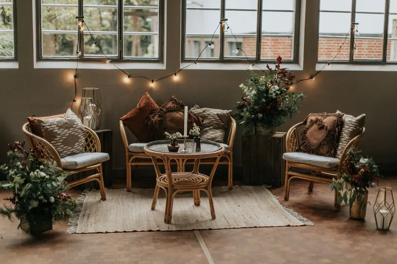 Lounge aus Rattansesseln, Sitzbank und rundem Tisch mit Kissen vor Sprossenfenstern