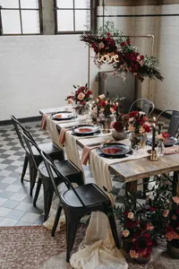 Schwarze Metallstühle an einem Holztisch mit roten Blumen in einem gefliesten Saal