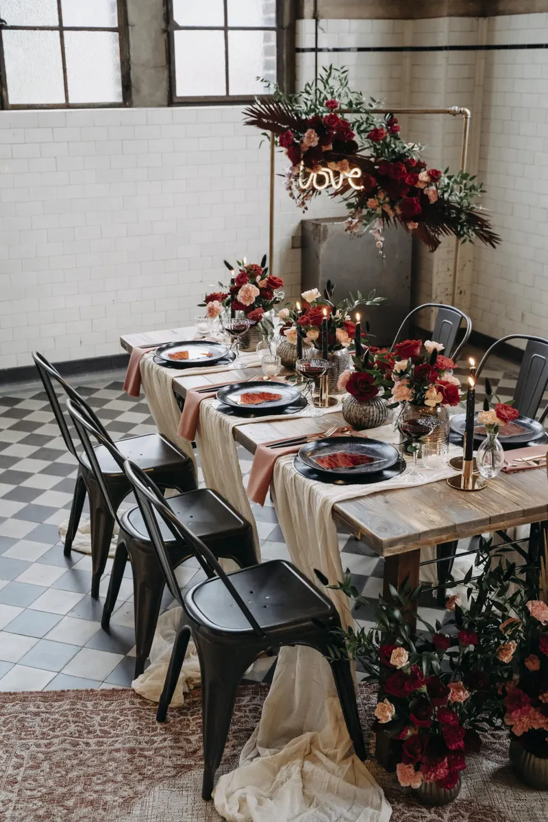Schwarze Metallstühle an einem Holztisch mit roten Blumen in einem gefliesten Saal