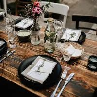 Dunkler Plankentisch mit schwarzen Tellern, Leinenservietten und Wildblumen