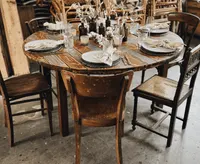 Zwei dunkle Rundtische mit Vintagestühlen und Trockenblumen