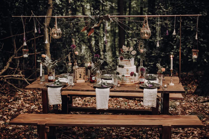 Holzsitzbank an einer gedeckten Tafel mit Hochzeitstorte im Wald