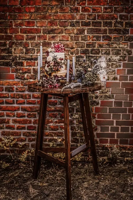 Dunkler Holzstehtisch mit Blumen vor einer Backsteinwand