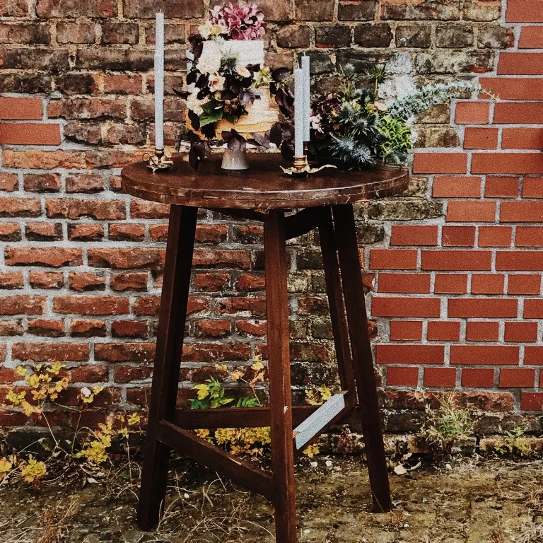 Stehtisch aus dunklem Holz mit Hochzeitstorte vor Backstein