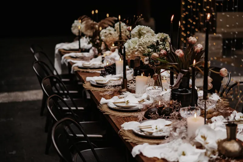 Dunkle Tafel mit weißen Blumen, Kerzen und schwarzen Stühlen