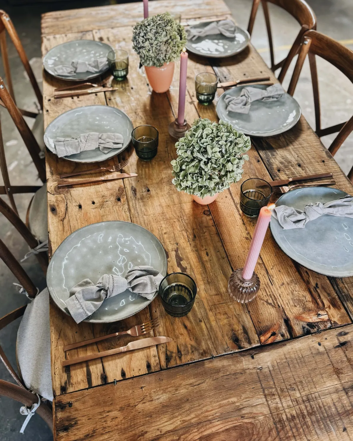 Tisch Finca aus grobem Holz mit grauen Tellern, Buchsbaum und rosa Kerzen