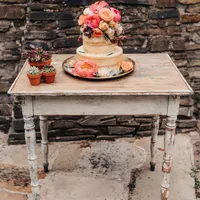 Weißer Vintage Trautisch mit dreistöckiger Torte und Sukkulenten vor Backstein